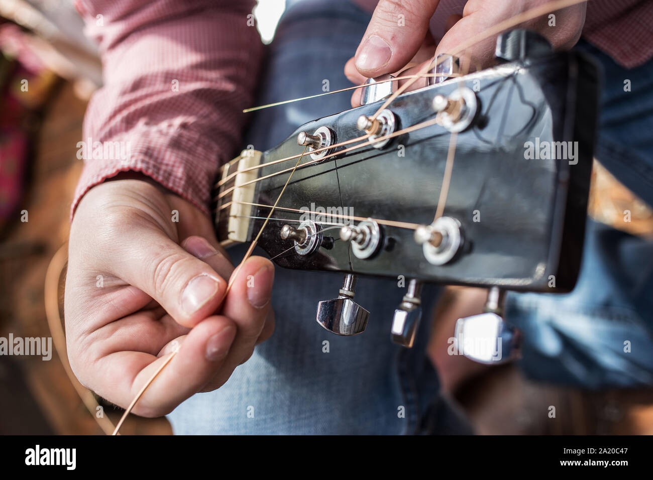 Un uomo in un plaid shirt tira di nuovo le corde di una chitarra chitarra acustica close-up Foto Stock