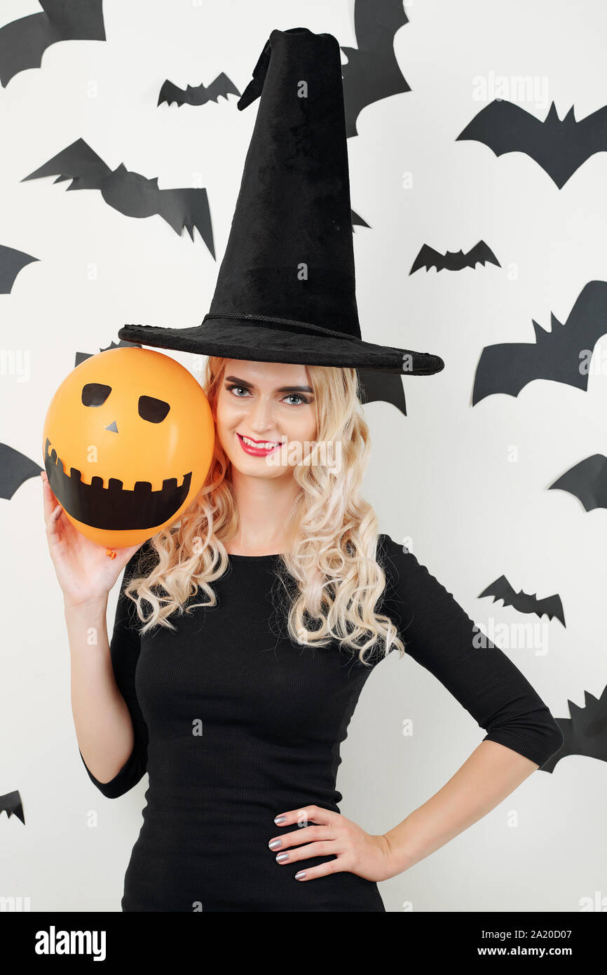 Ritratto di fiduciosa piuttosto giovane donna in costume maga che mostra il palloncino arancione con occhi dipinti e spaventoso sorriso toothy Foto Stock