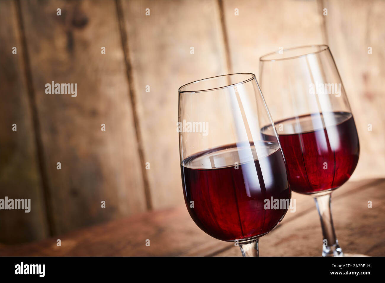 Due eleganti wineglass di vino merlot affiancati su legno rustico sfondo con spazio copia in corrispondenza di un angolo inclinato Foto Stock