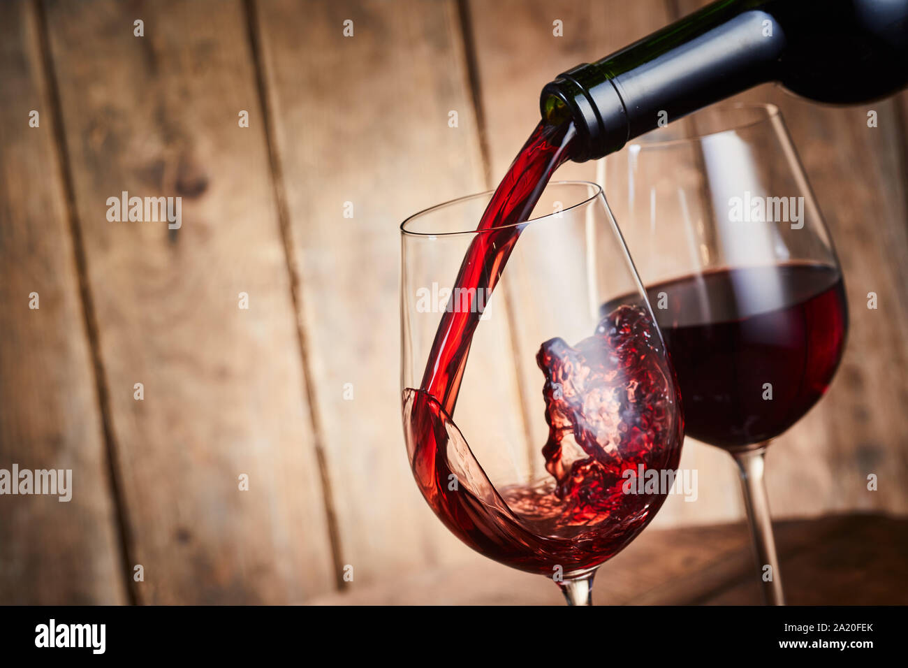 Il vino rosso è versata in un elegante wineglass in una chiusura sul collo della bottiglia su legno con copia spazio e congelare il movimento dello splash ancora Foto Stock