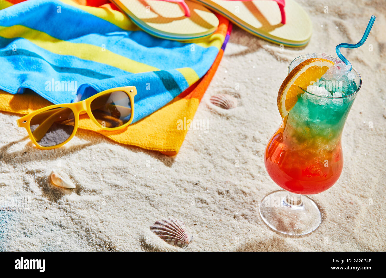 Colorati cocktail esotici su di una spiaggia di sabbia a fianco di un telo da spiaggia, infradito e occhiali da sole giallo concettuale del rifugio estivo su un isola tropicale Foto Stock