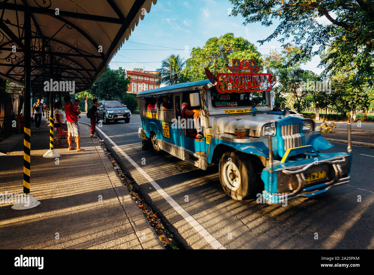 Manila, Filippine - 10 Novembre 2018: la gente comune di attendere per il trasporto a una fermata del bus mentre il blu Jeepney passa da novembre 10, 2018 a Manila Foto Stock
