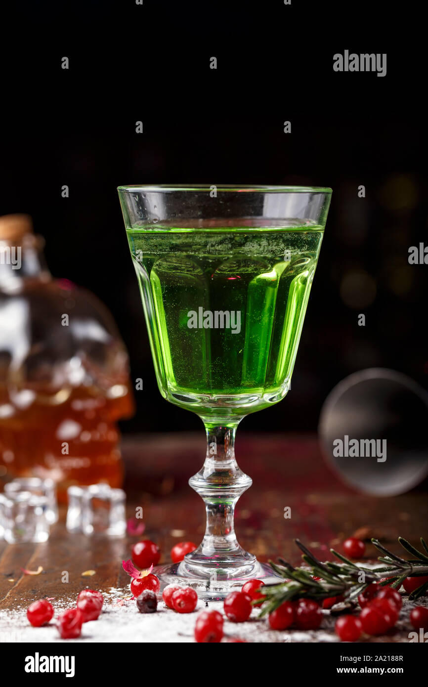 Cocktail verde sulla base di assenzio in un elegante vintage vetro su di un legno marrone. sfondo dello zucchero bianco e mirtilli sono sparsi nei dintorni Foto Stock