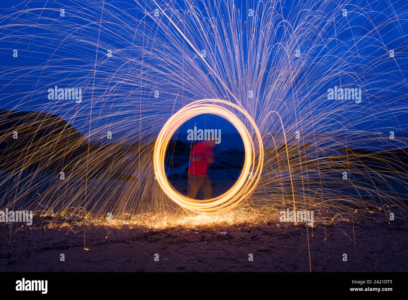 Un uomo che fa circolare la luce di filatura dipinto con lana di acciaio durante la notte sulla spiaggia. Foto Stock
