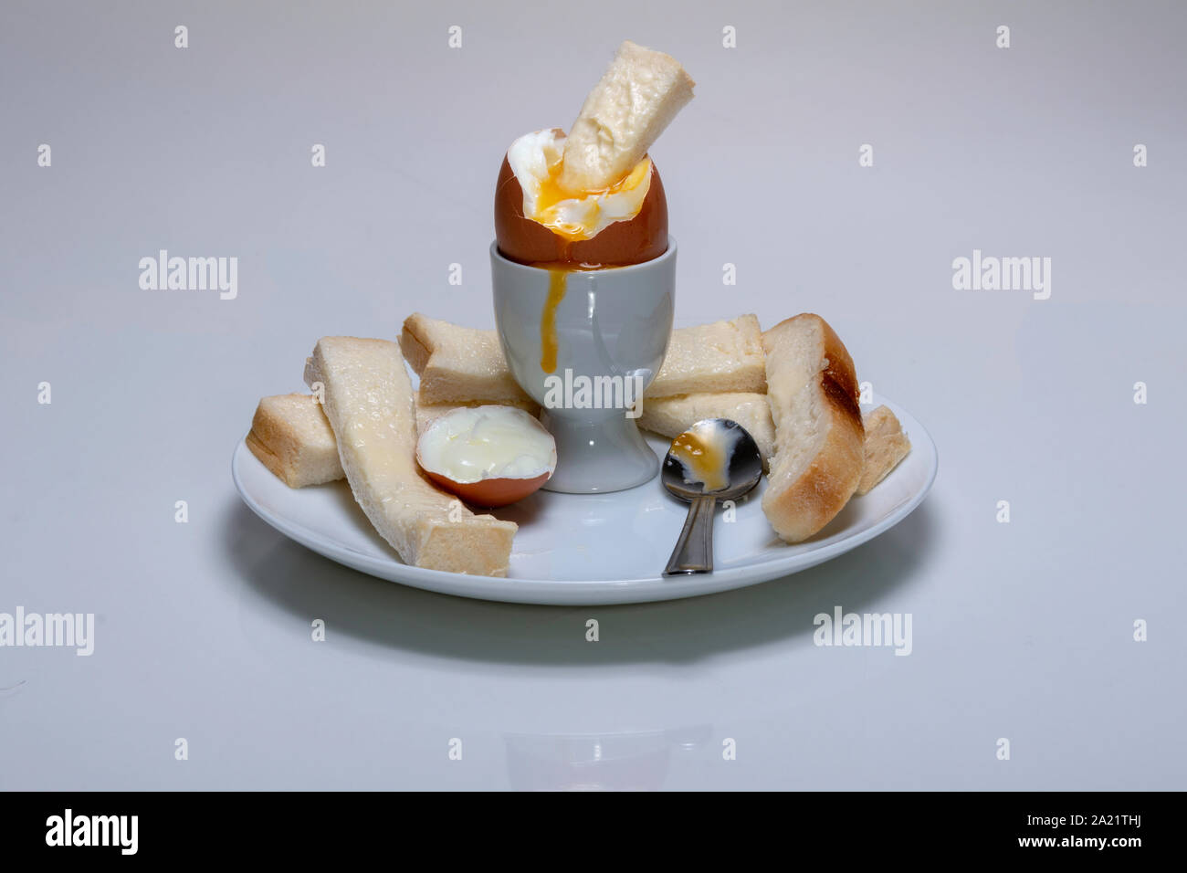 Soft boiled pollo uovo, in un uovo cup con pane imburrato, soldati e un cucchiaio da tè in appoggio su una piastra Foto Stock