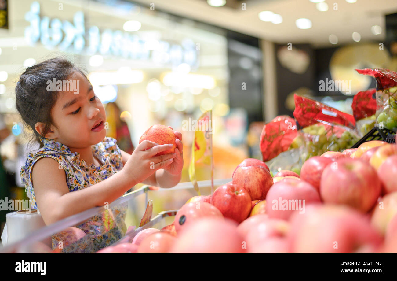 Asian bambina scegliendo un Apple in un negozio di alimentari o supermarket Foto Stock