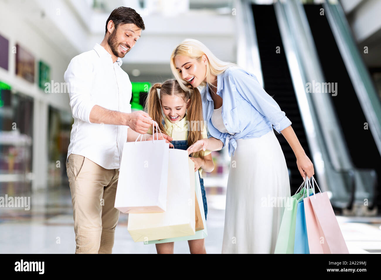 Famiglia eccitato guardando in borse per lo shopping a acquistato vestiti in piedi nel centro del centro commerciale. Ipermercato soddisfatti i clienti Foto Stock