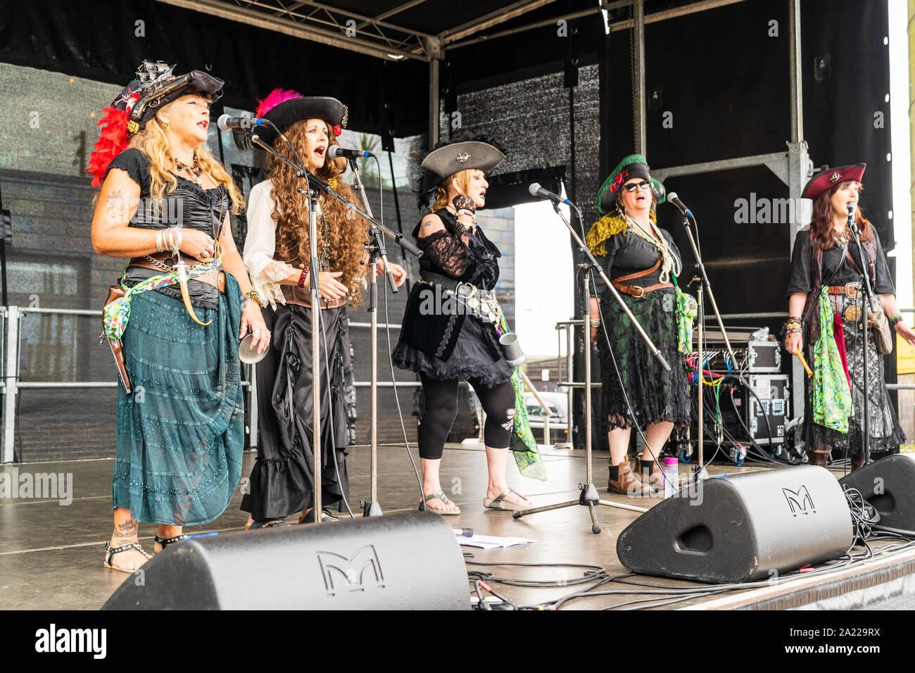 Giorno pirata in Hastings. Armonia al femminile, il gruppo Rattlebag cantanti sulla scena sonora in pieno costume pirata, stando in piedi in linea di cantare in microfoni. Foto Stock