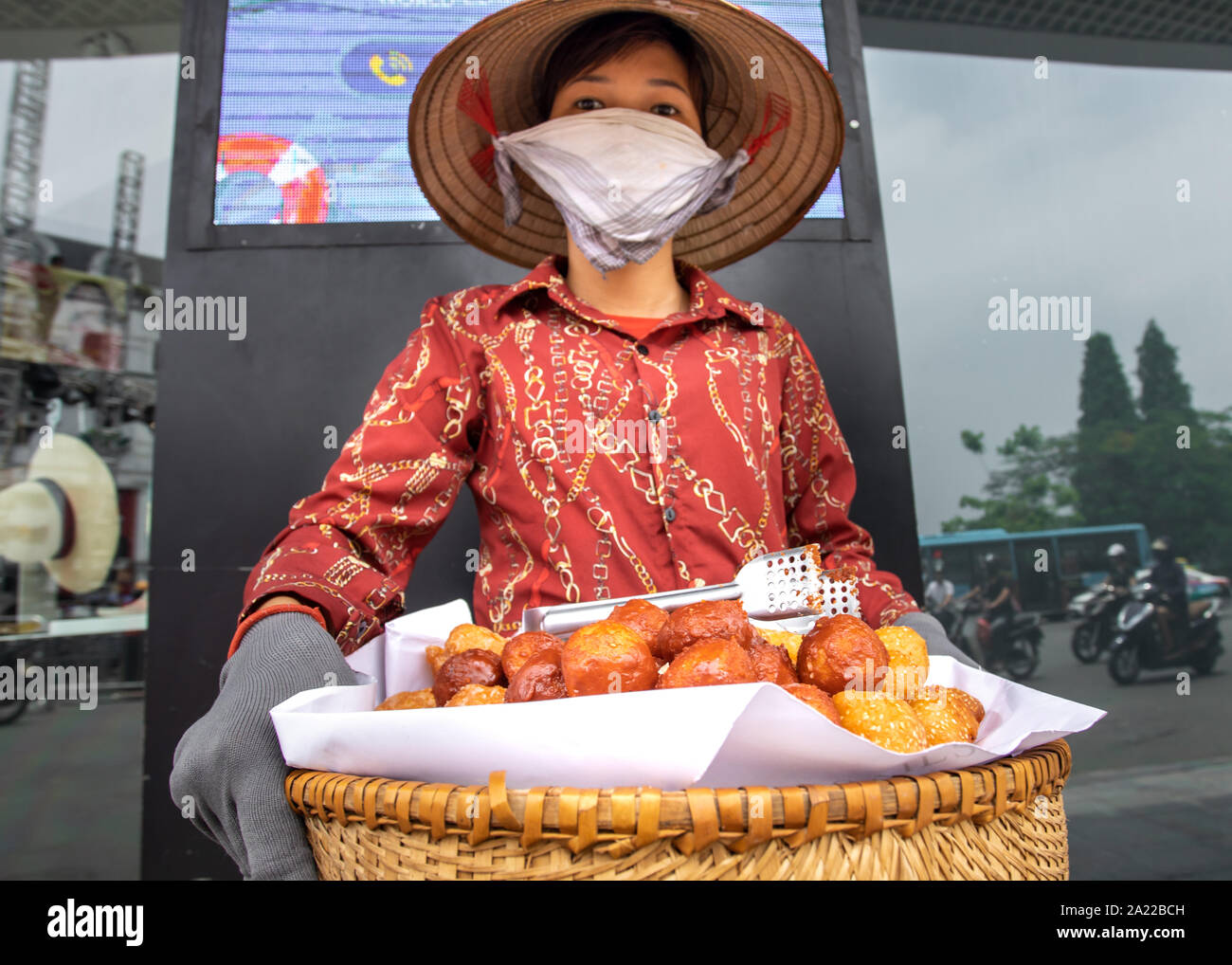 Donna con maschera di inquinamento di vendita vietnams tradizionale cibo in strada di Hanoi. Foto Stock