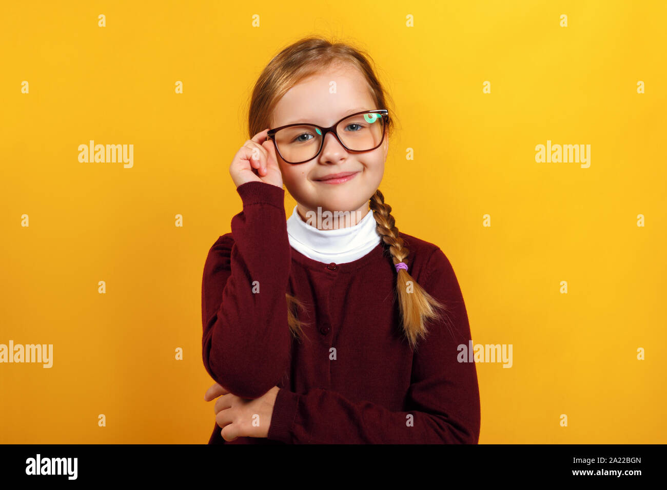 Piccolo e intelligente girl School girl corregge gli occhiali. Un bambino in un maglione rosso su sfondo giallo. Foto Stock
