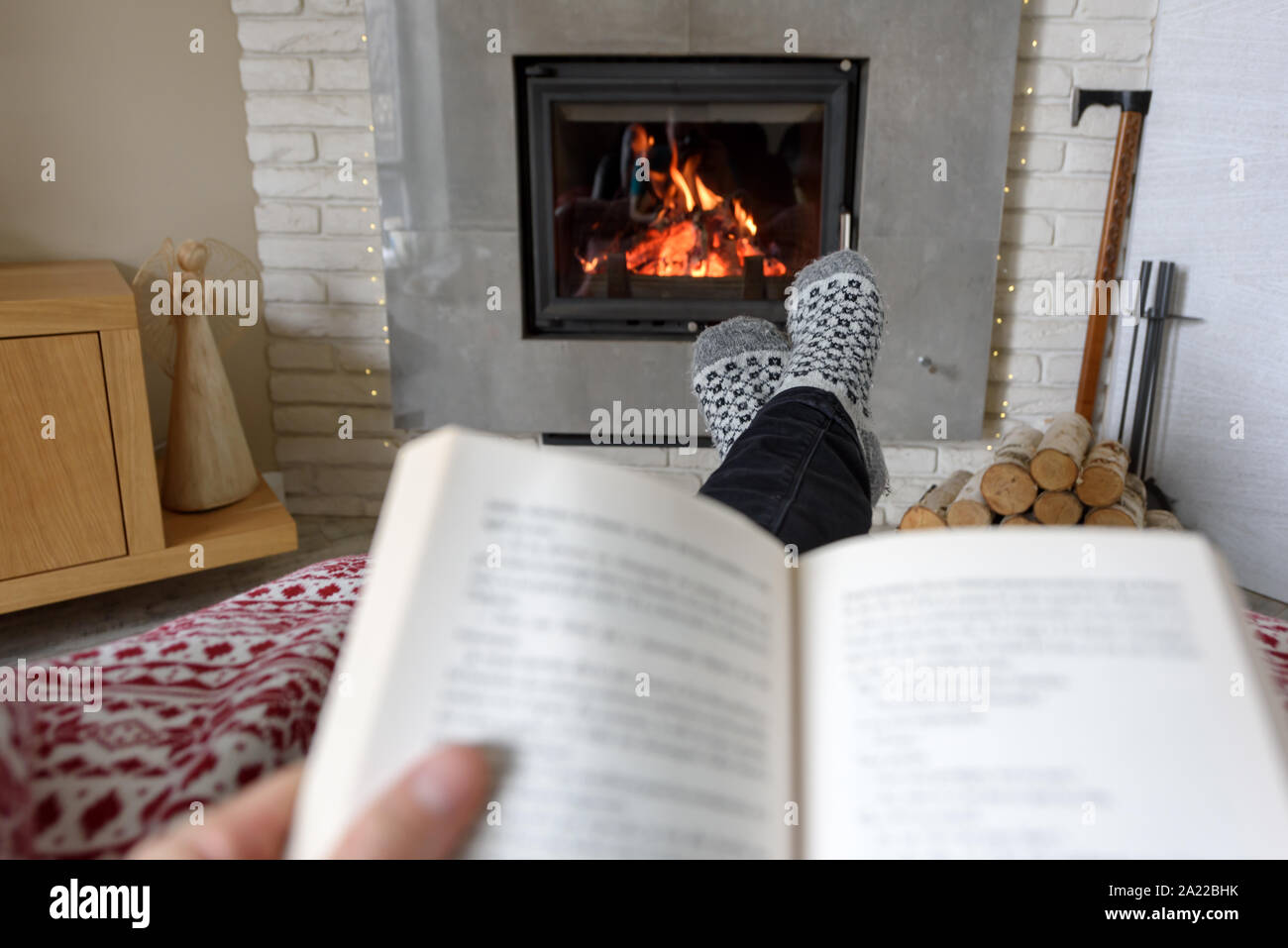 Concetto di Hygge con il libro aperto in mano uomo vicino al caminetto Foto Stock