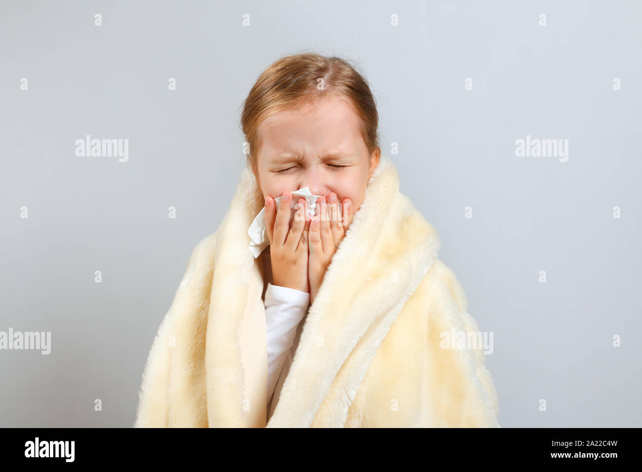 Bambina soffia il naso, avvolto in un plaid, su sfondo grigio. Foto Stock