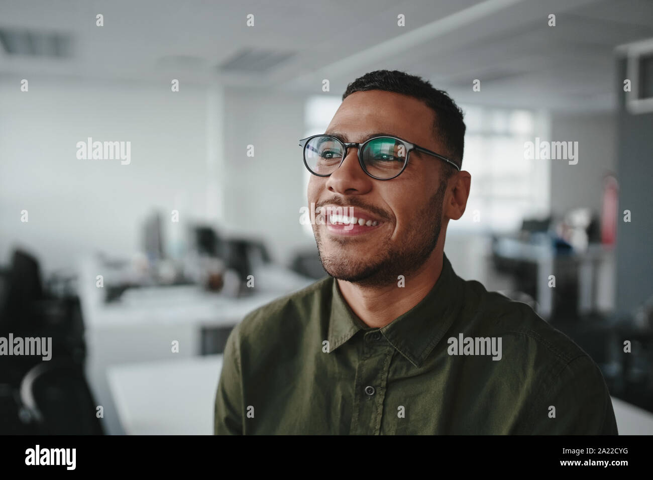 Ritratto di un ragionato sorridente giovane moderno business man in ufficio che guarda lontano Foto Stock