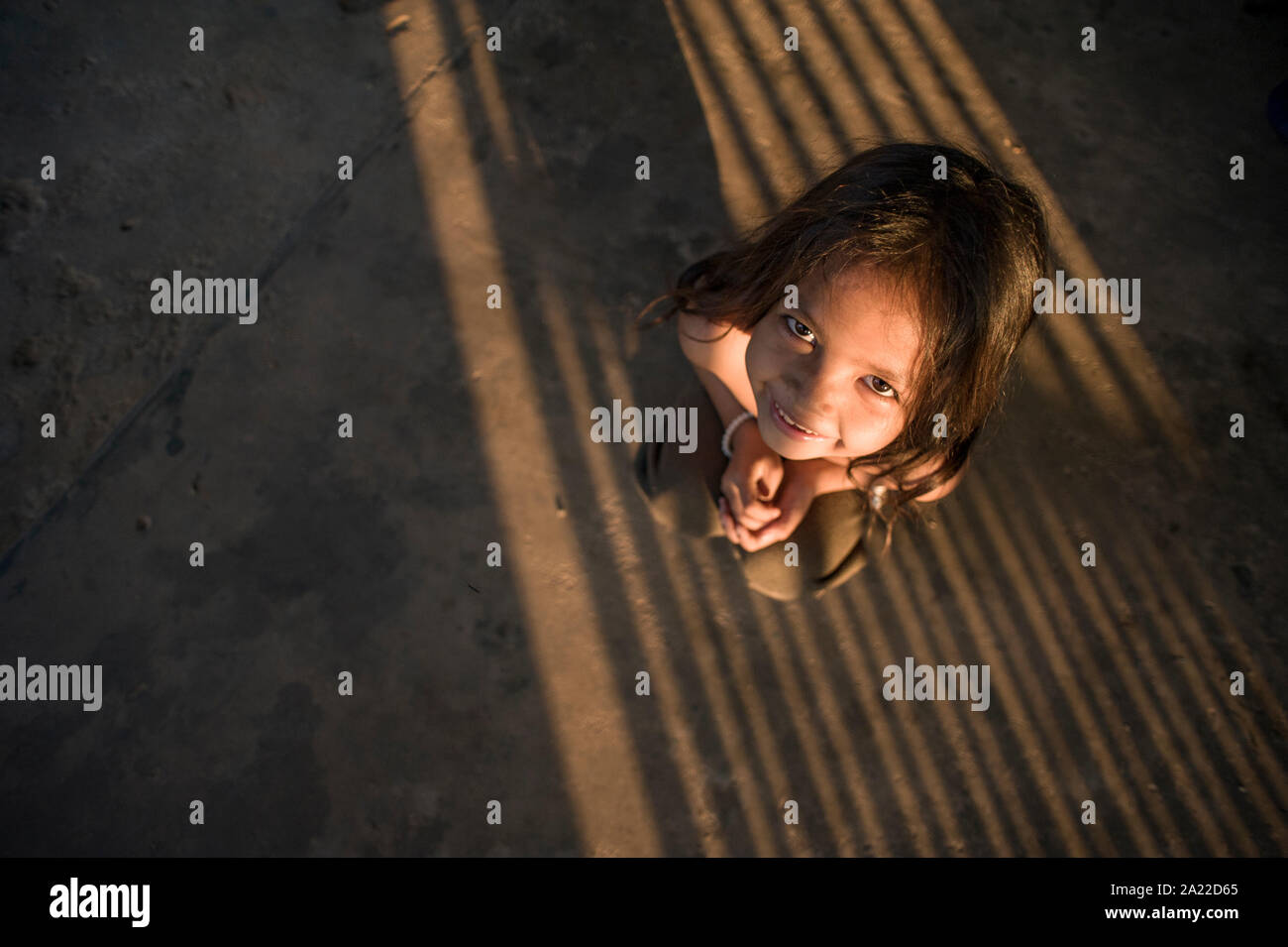 Piccolo dolce ragazza cambogiano accovacciato sul terreno ombreggiato Foto Stock