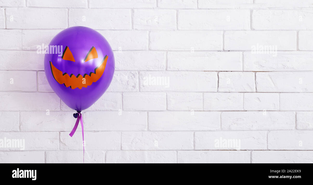 Concetto di Halloween. Celebrando il palloncino viola con il male sorriso sul bianco muro di mattoni di sfondo, panorama, spazio di copia Foto Stock