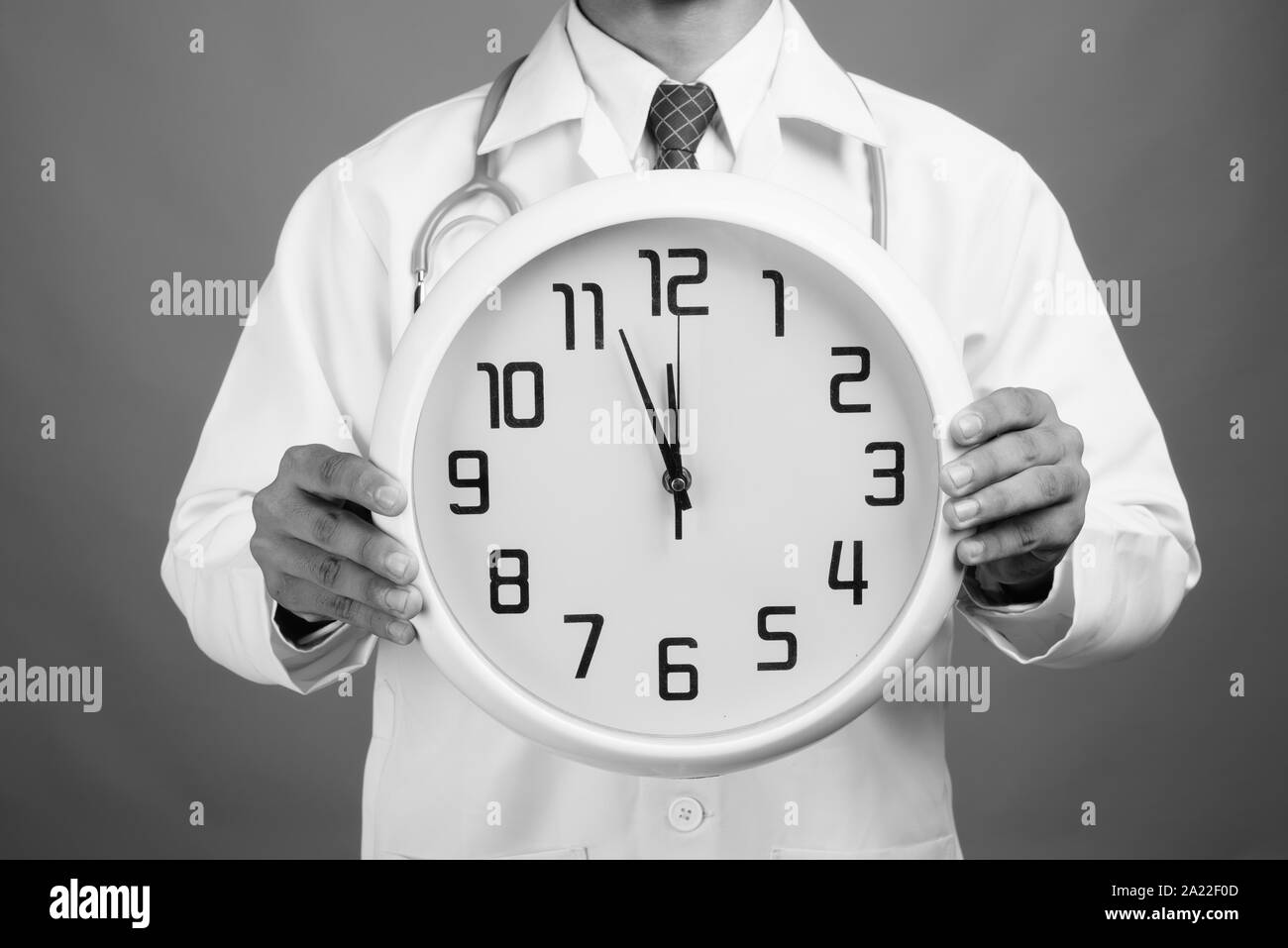 Le mani del giovane uomo indiano medico tenendo orologio da parete contro uno sfondo grigio Foto Stock