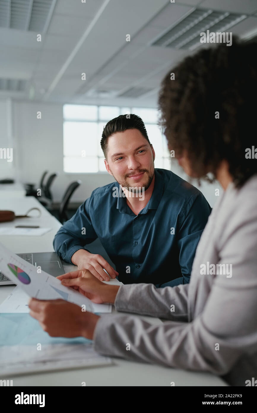 Sorridente imprenditore giovane seduto con il suo collega di sesso femminile al tavolo analizzando i report finanziari in office Foto Stock