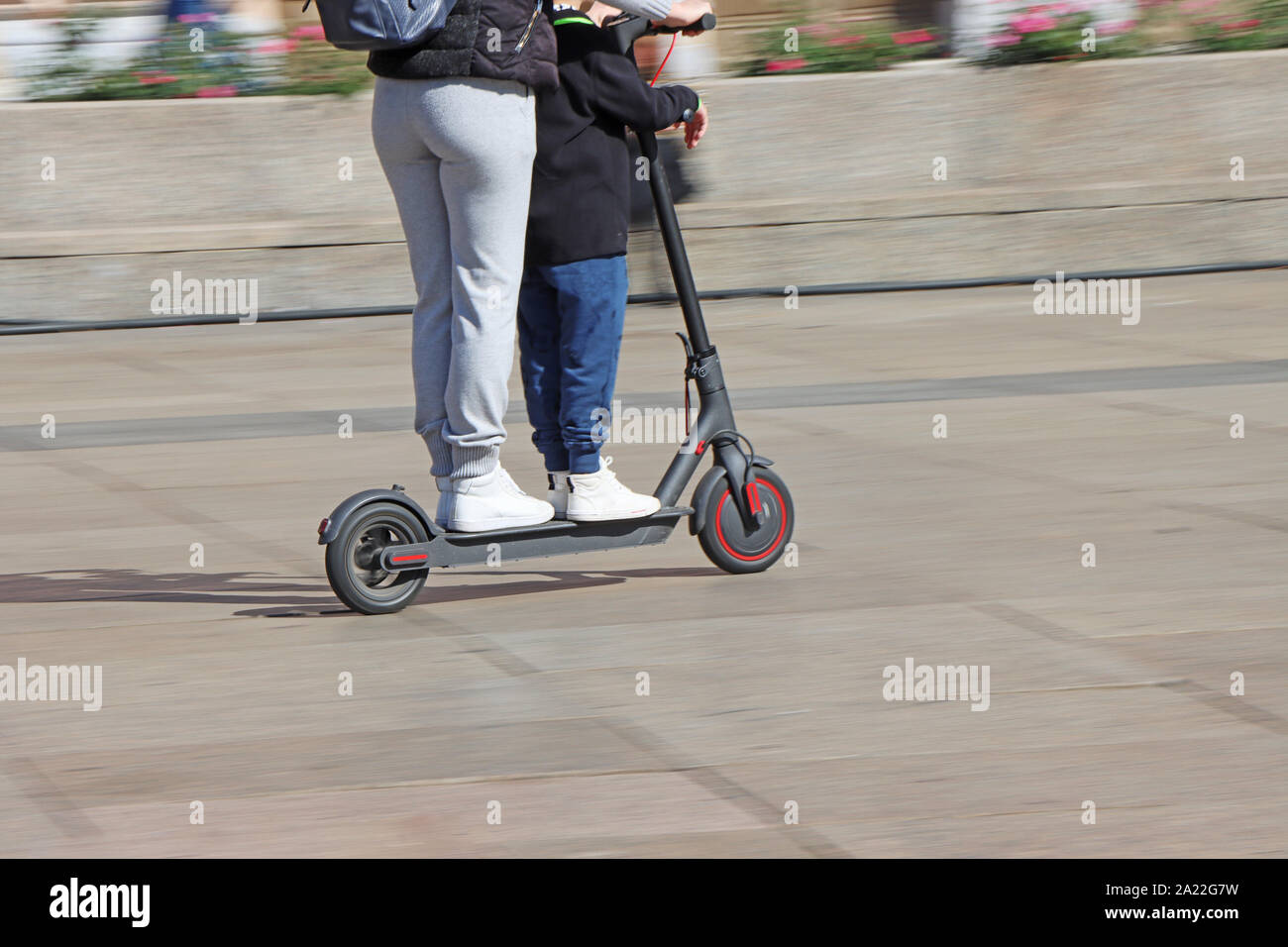 Madre e figlio di equitazione calcio elettrico scooter presso la piazza della città, movimento sfocato Foto Stock