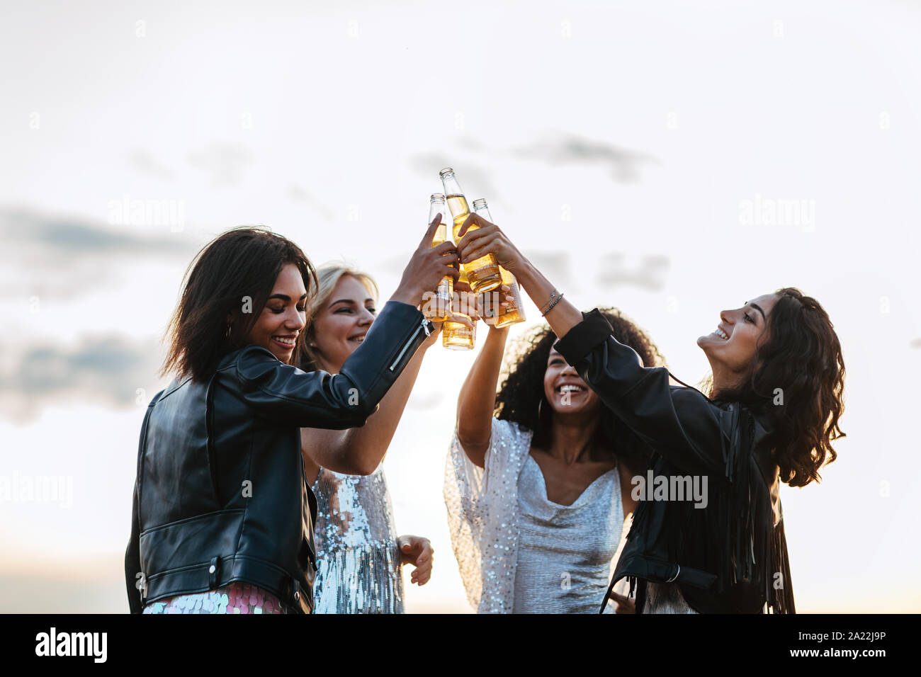 Quattro amici felice la tostatura con bottiglie di birra al tramonto Foto Stock