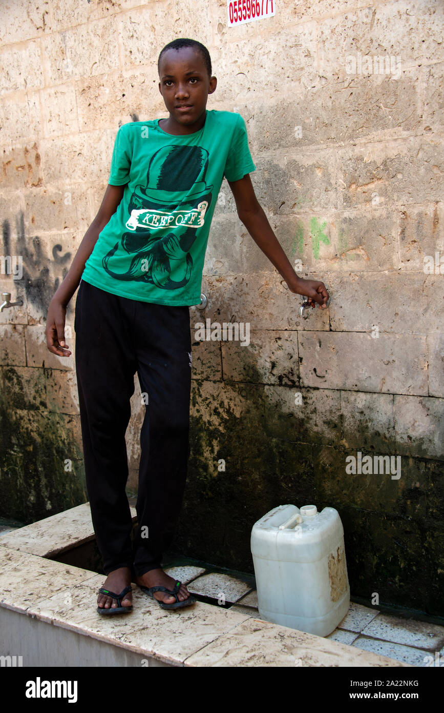 Giovane ragazzo il riempimento della benna all'aperto con rubinetto di acqua di Jeddah, Arabia Saudita Foto Stock