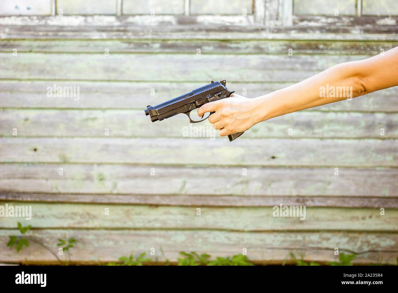 La mano di una donna con una pistola isolate su un vecchio muro sfondo, all'aperto Foto Stock