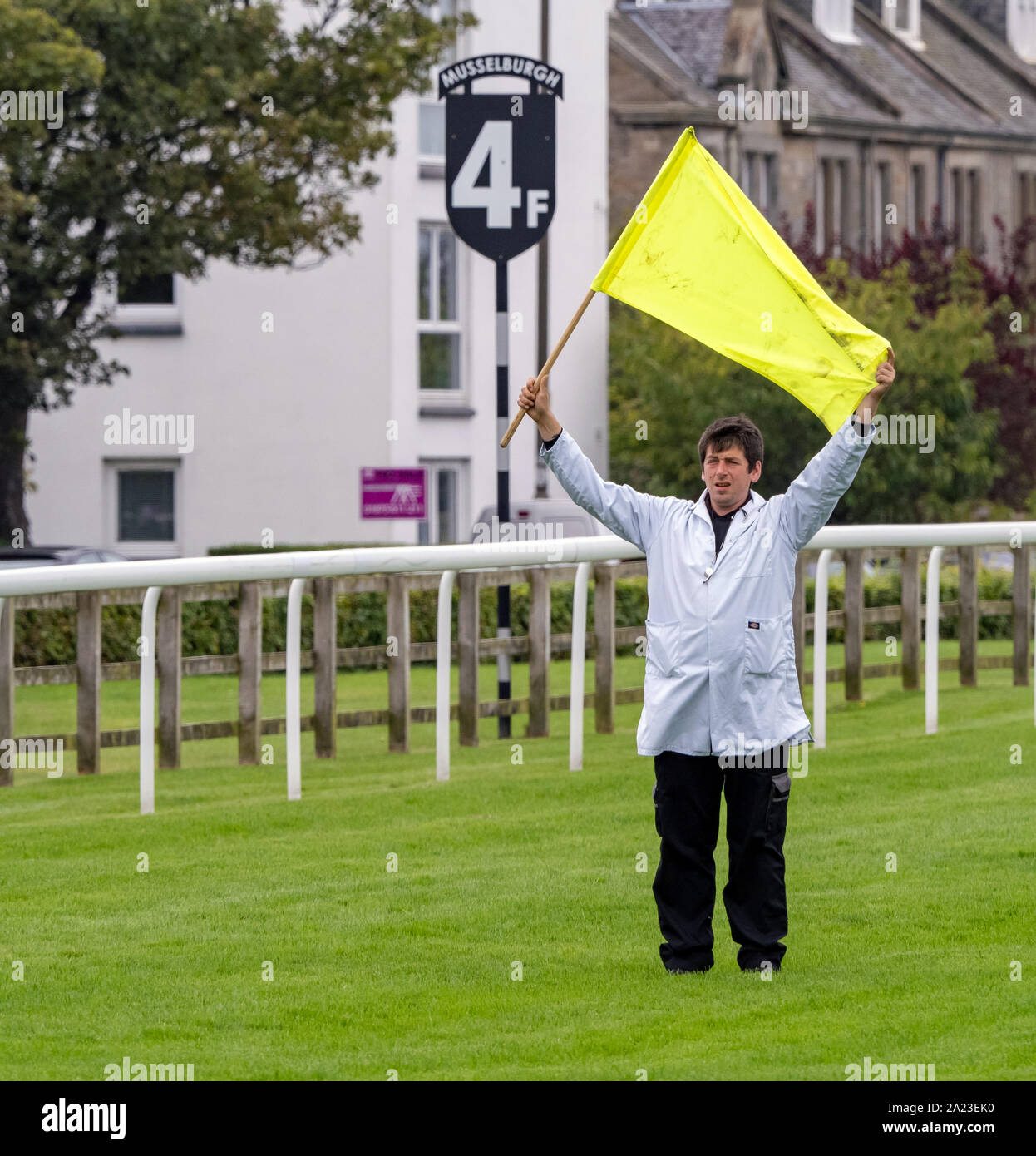 La bandiera gialla uomo prima di iniziare una gara piatta a Musselburgh Racecourse. Foto Stock