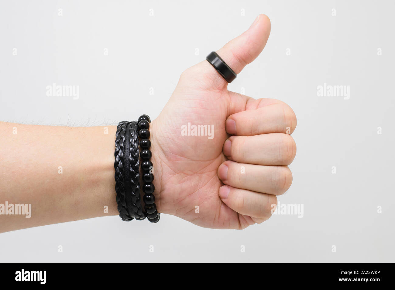 Pollice alzato la mano di un uomo bianco che indossa una spessa anello nero sul  pollice e alcuni nero accessori da polso. Black Rock'n'roll accessori.  Backgroun bianco Foto stock - Alamy