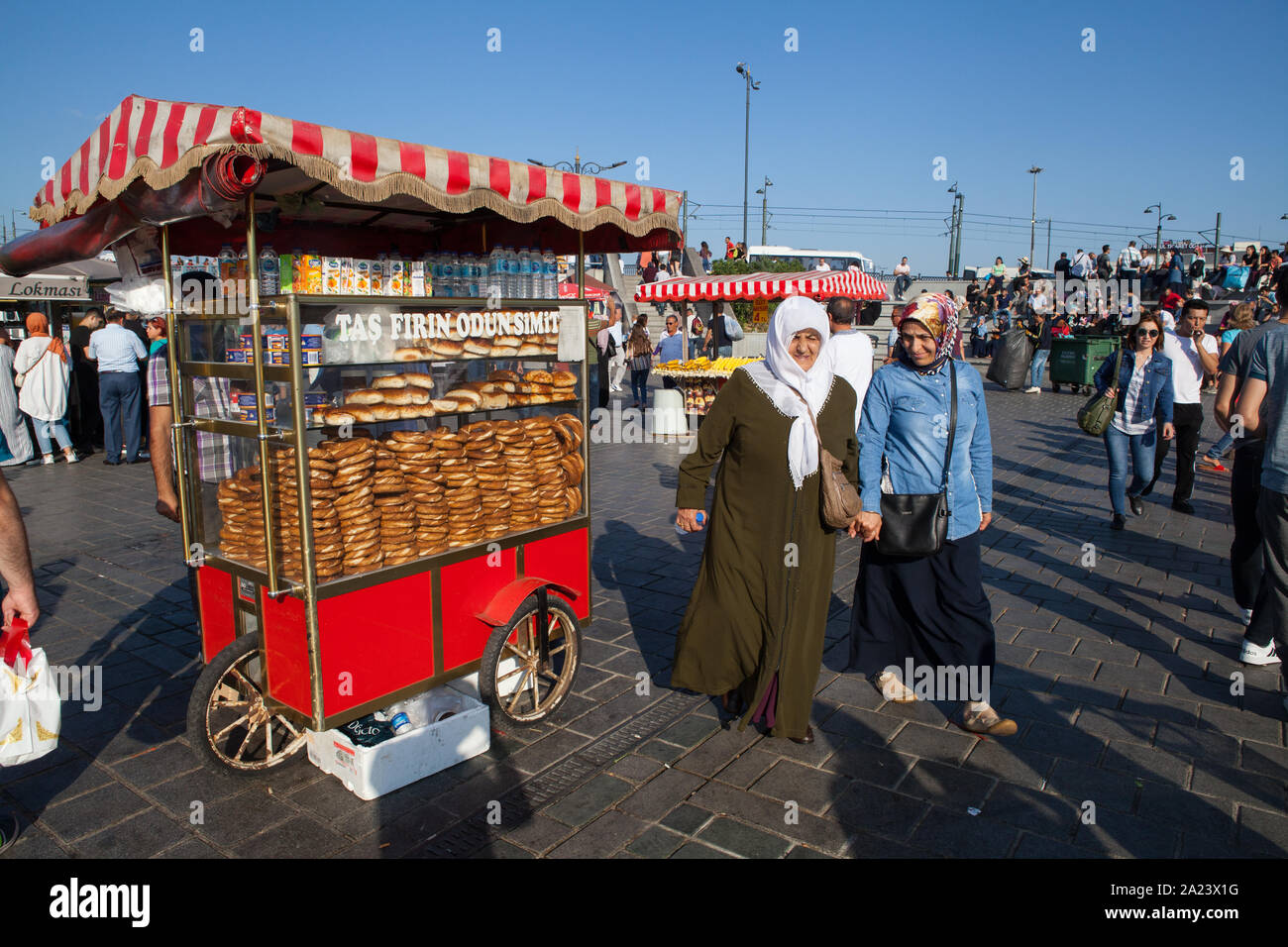 Le donne musulmane a piedi da un alimento bancarella vendendo simit (pane turco) sul lungomare vicino al Ponte di Galata Foto Stock