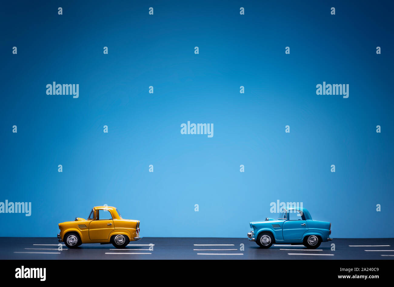 Due automobili giocattolo sulla strada una dopo l'altra. Uno è blu è colorata in giallo. Su uno sfondo blu. Foto Stock