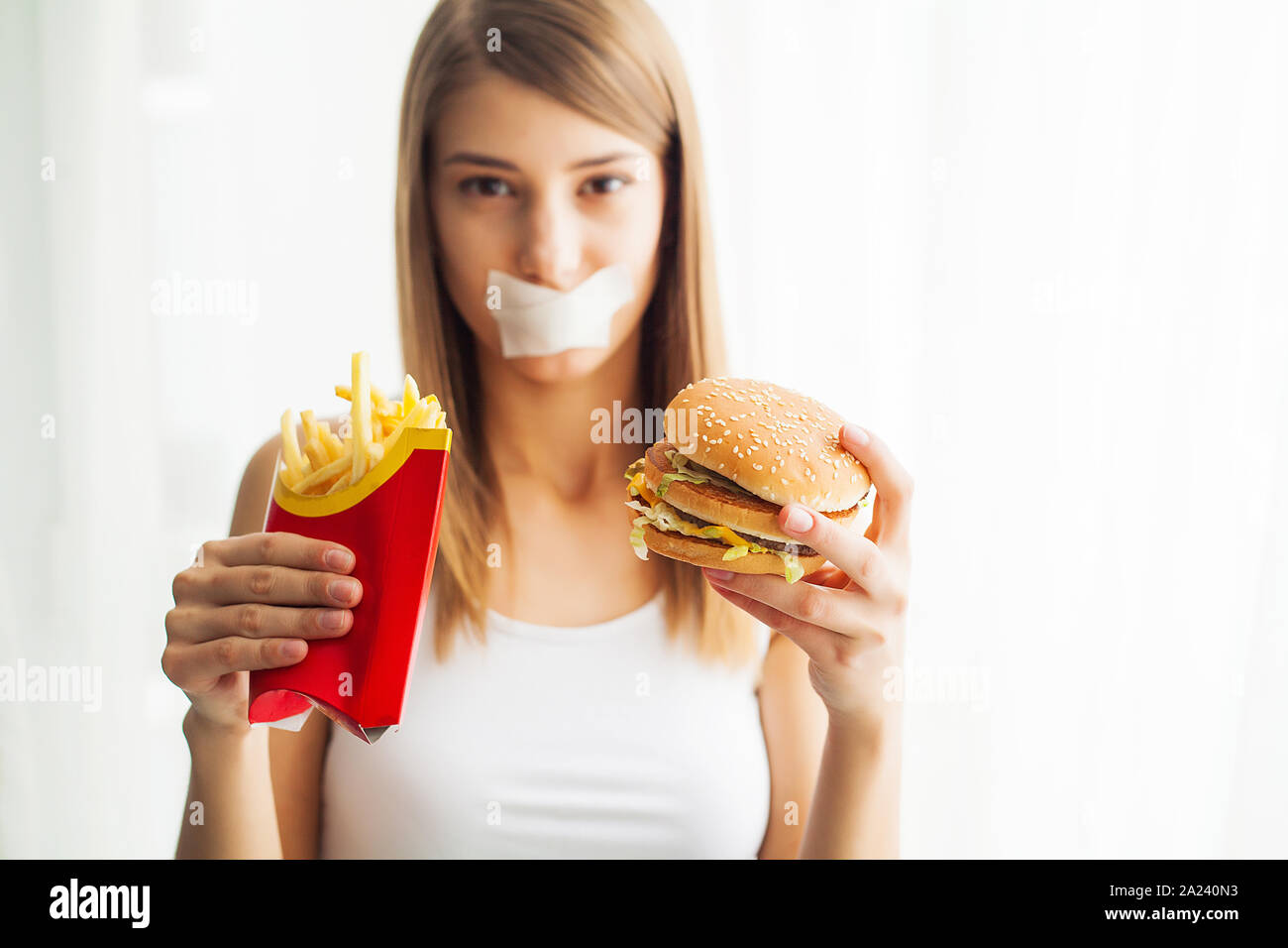 La dieta. Ritratto donna vuole mangiare un hamburger ma bloccato skochem bocca, il concetto di dieta, cibo spazzatura, volontà in nutrizione Foto Stock