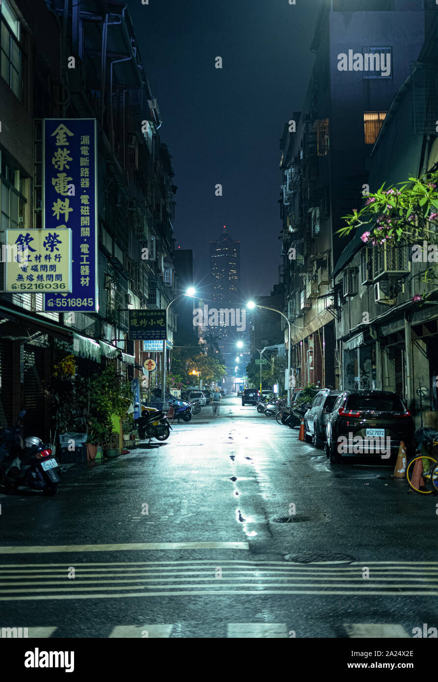 Kaohsiung, Taiwan: un buio, vicolo urbano in una notte piovosa con la Tuntex Sky Tower 85 alla fine della strada. Luci che riflettono su asfalto bagnato Foto Stock