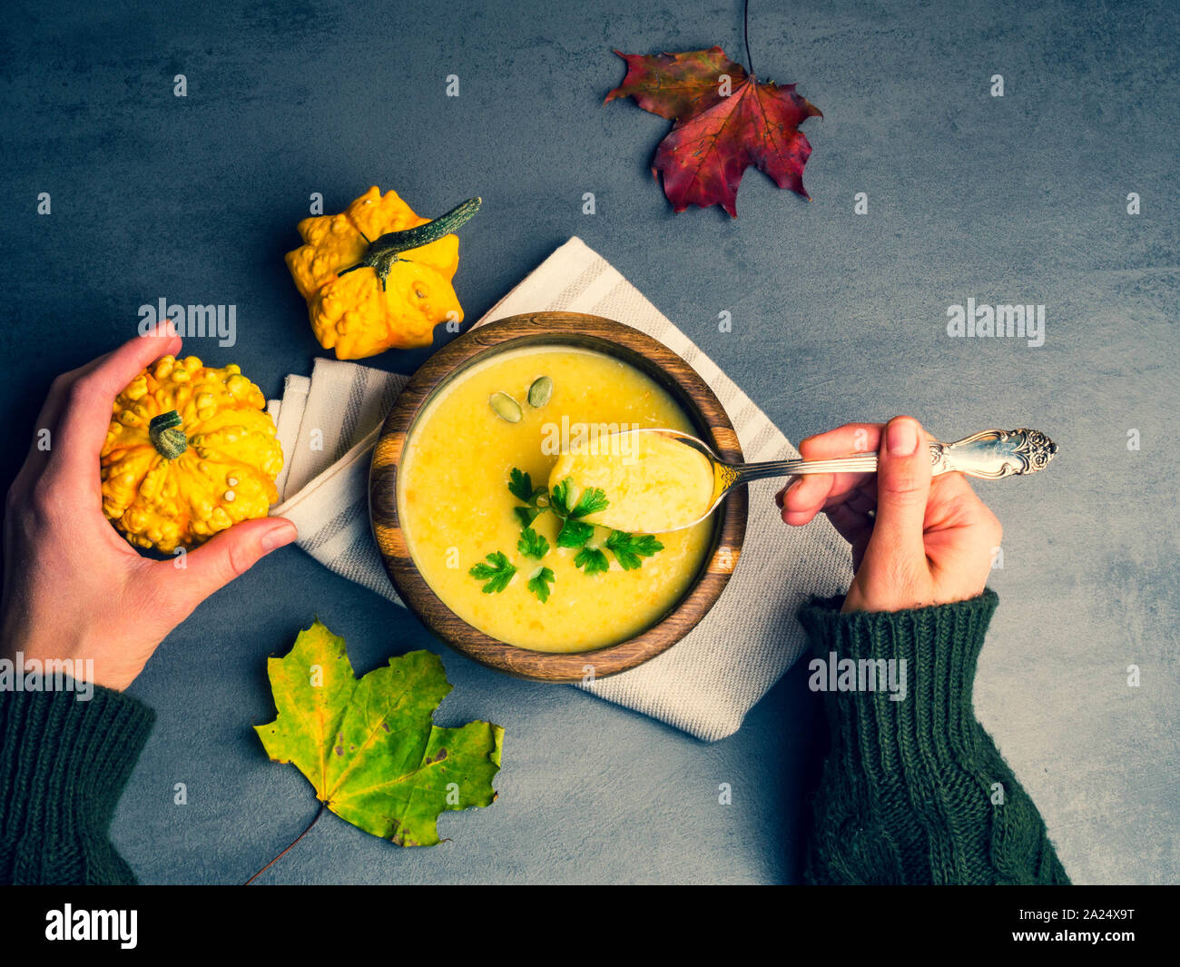 Persona che tiene la coppa con una deliziosa zuppa di zucca, il gufo di zucca e carota minestra in crema nelle mani delle donne. Autunno Caldo zuppa vegana concetto, con fogliame Foto Stock