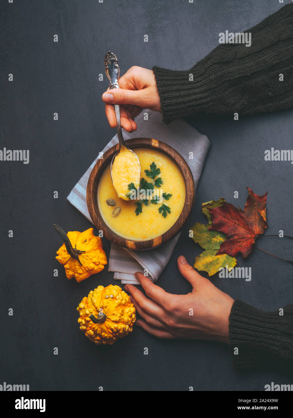 Persona che tiene la coppa con una deliziosa zuppa di zucca, il gufo di zucca e carota minestra in crema nelle mani delle donne. Autunno Caldo zuppa vegana concetto, con fogliame Foto Stock