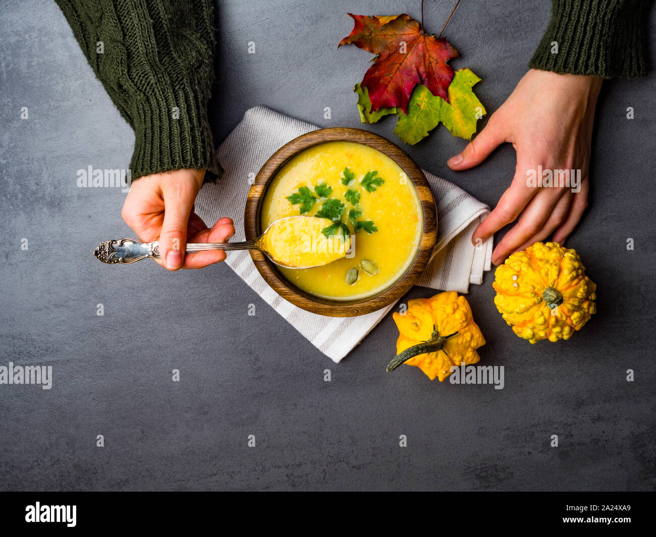 Persona che tiene la coppa con una deliziosa zuppa di zucca, il gufo di zucca e carota minestra in crema nelle mani delle donne. Autunno Caldo zuppa vegana concetto, con fogliame Foto Stock