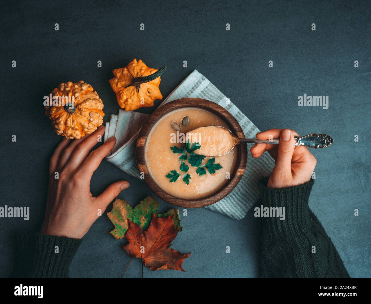 Persona che tiene la coppa con una deliziosa zuppa di zucca, il gufo di zucca e carota minestra in crema nelle mani delle donne. Autunno Caldo zuppa vegana concetto, con fogliame Foto Stock