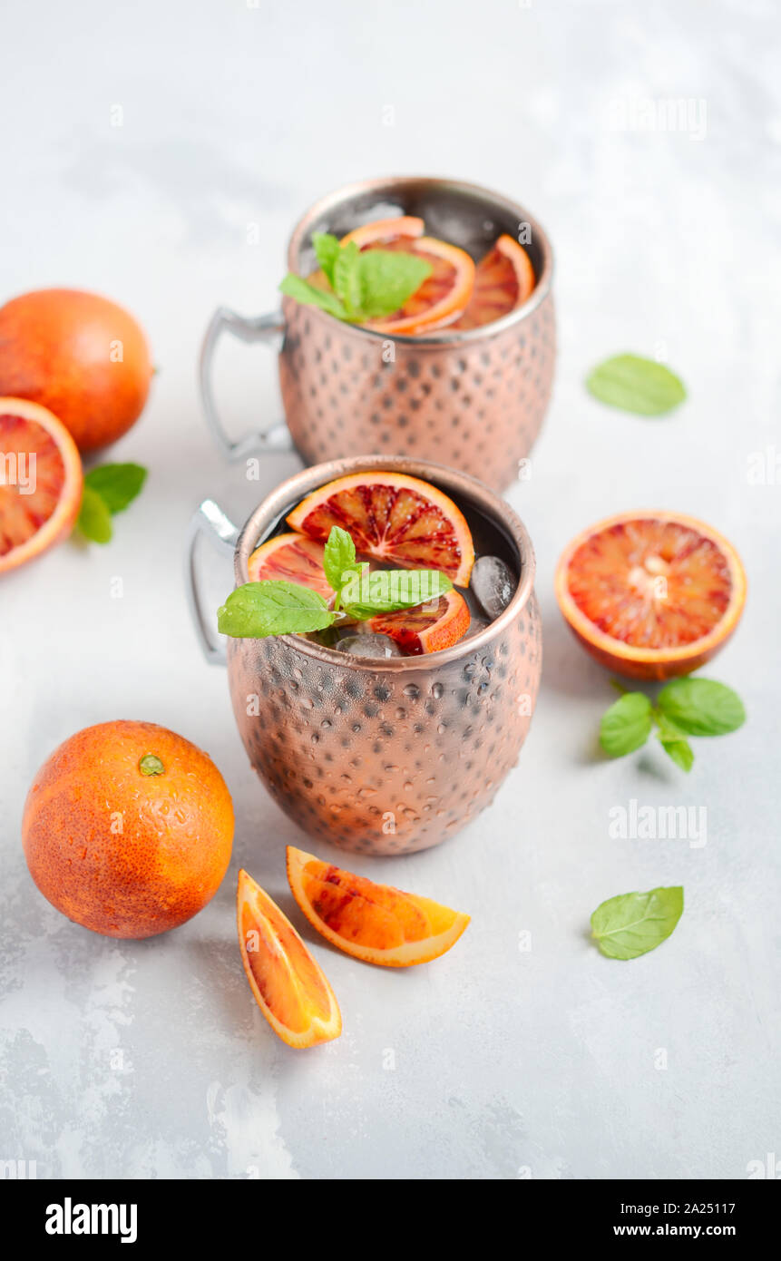 Arancio sanguigno Moscow mule cocktail alcolici con foglie di menta fresca e ghiaccio in tazze di rame su un cemento grigio Sfondo. Foto Stock