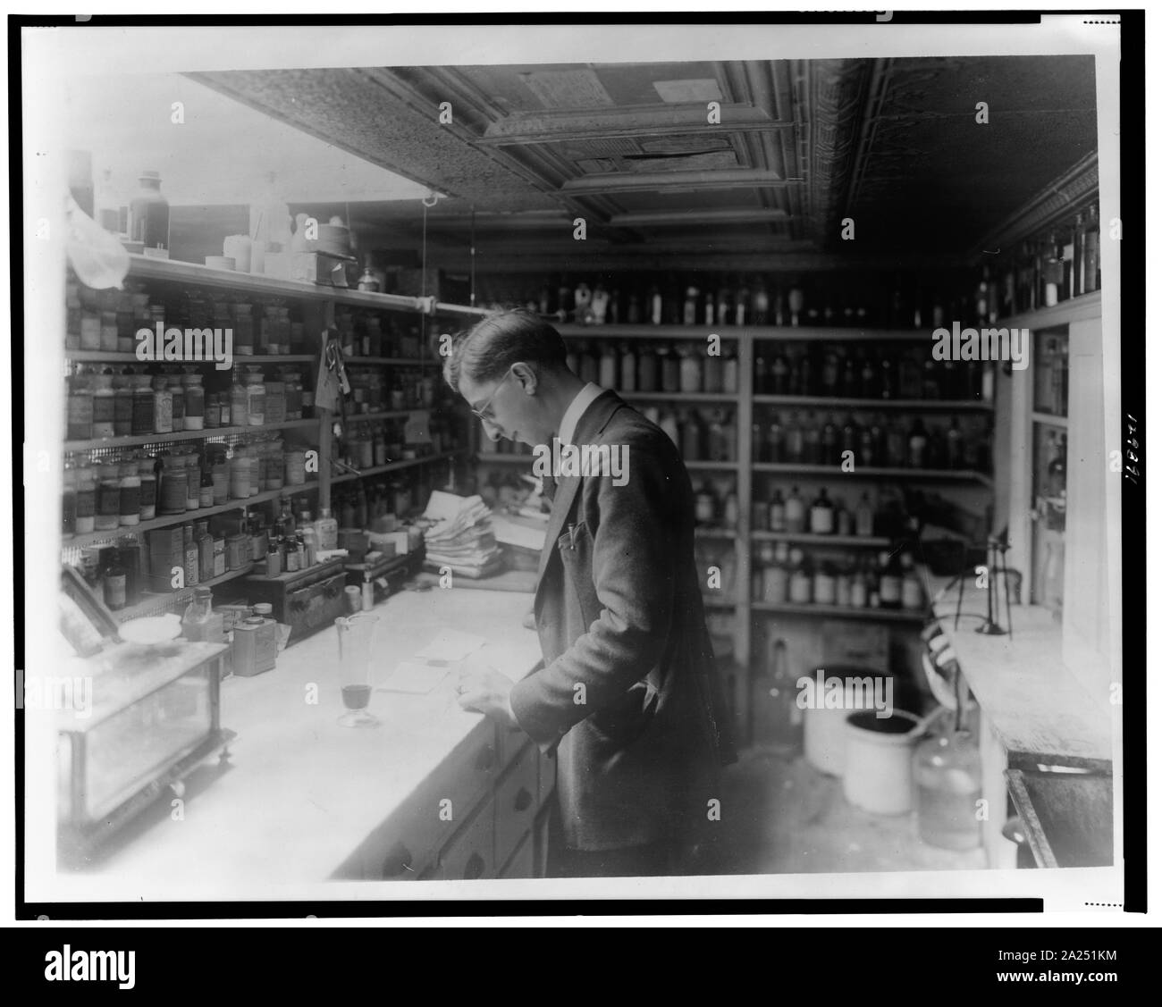 Il farmacista a persone di Drug Store, n. 5, 8 e H strade, N.E., Washington D.C., guardando a prescrizioni() sul contatore in camera rivestita con ripiani di bottiglie di farmacia Foto Stock
