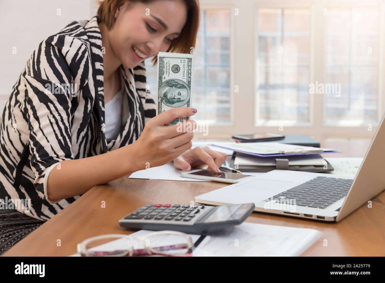 Business donna utilizzando smart phone e holding us dollari in contanti per pagare pagamenti online in cafe. Foto Stock