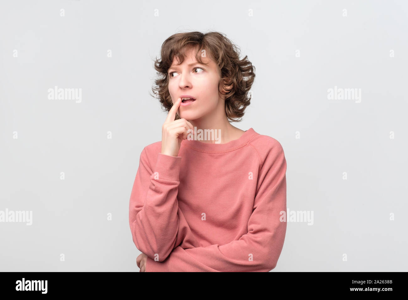 Giovane donna ricci di pensare e meditare su qualcosa con il suo dito sul mento. Studio shot Foto Stock