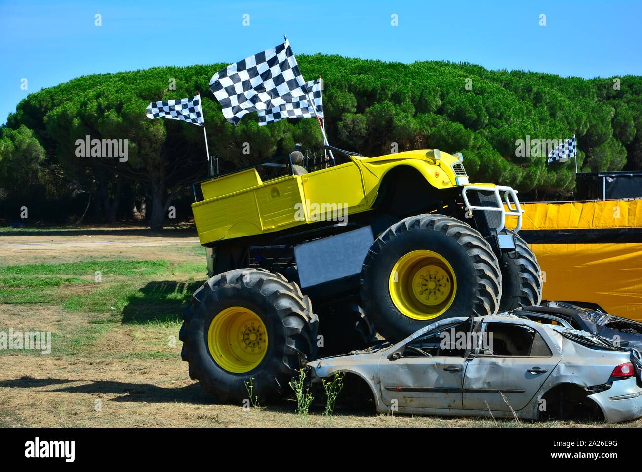 Uno giallo Monster Truck è in piedi su due vetture tritato prima di alberi verdi con cielo blu Foto Stock