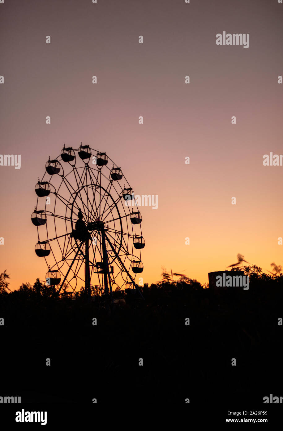 Silhouette di una ruota panoramica Ferris a sunrise (tramonto del sole su uno sfondo di alberi ed erba. Bellissimo sfondo con copia spazio. Foto Stock