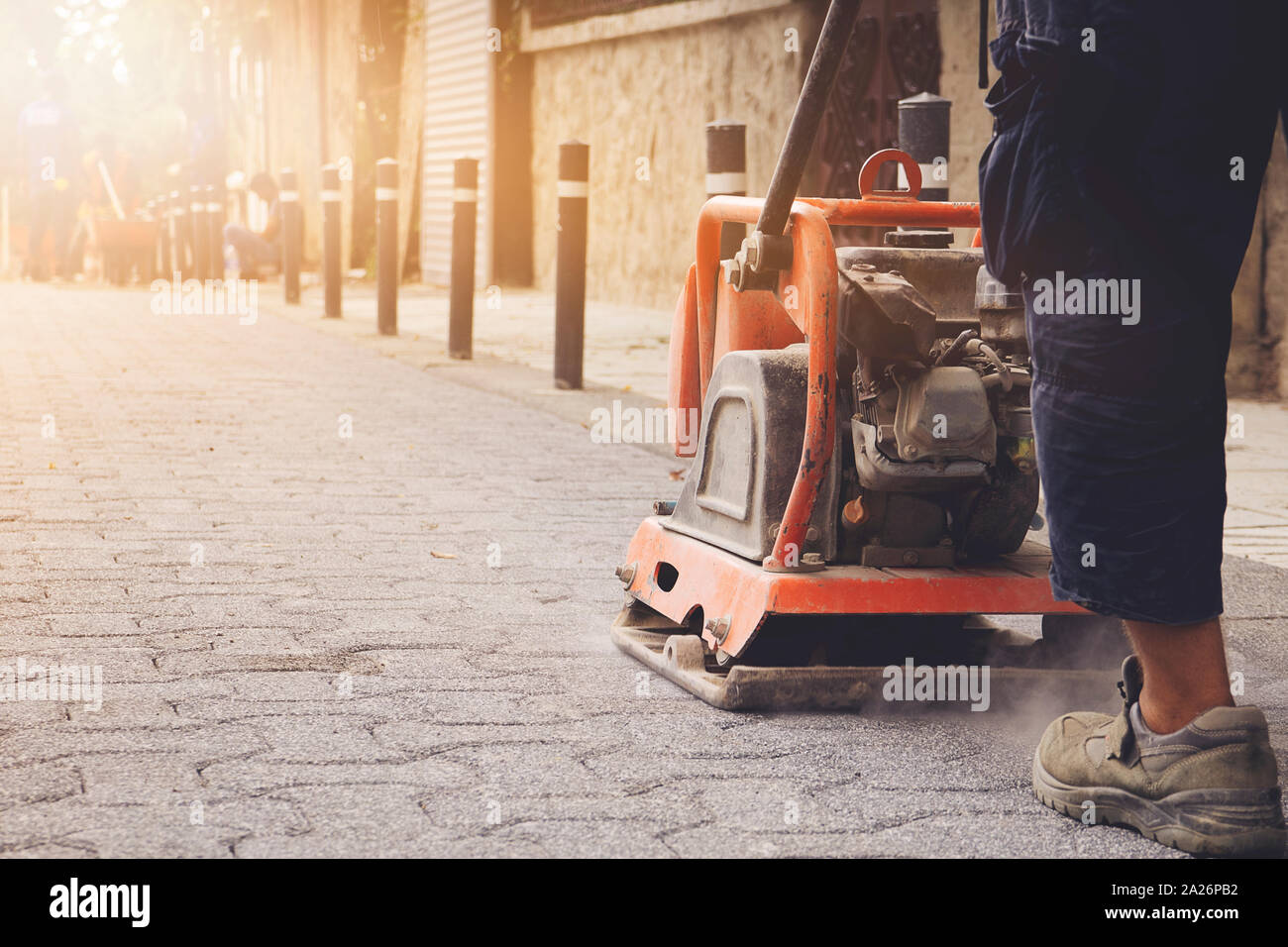 La piastra vibrante sito in costruzione. Lavoratori edili installazione e predisposizione di elementi prefabbricati in calcestruzzo Cemento pietra per strada in corrispondenza del luogo di costruzione. Foto Stock