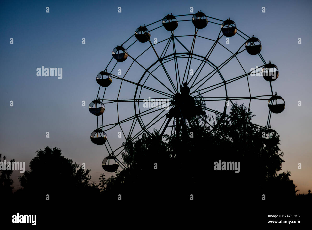 Silhouette di una ruota panoramica Ferris a sunrise (tramonto del sole su uno sfondo di alberi ed erba. Bellissimo sfondo con copia spazio. Foto Stock