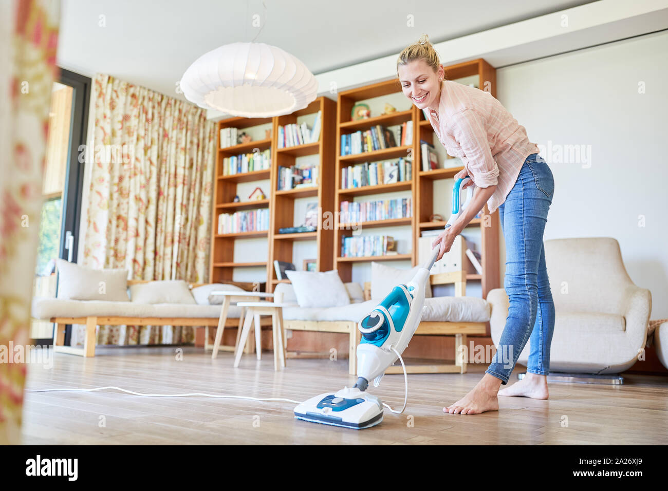 La casalinga come una donna delle pulizie con un pulitore a vapore nel soggiorno presso la pulizia del pavimento Foto Stock