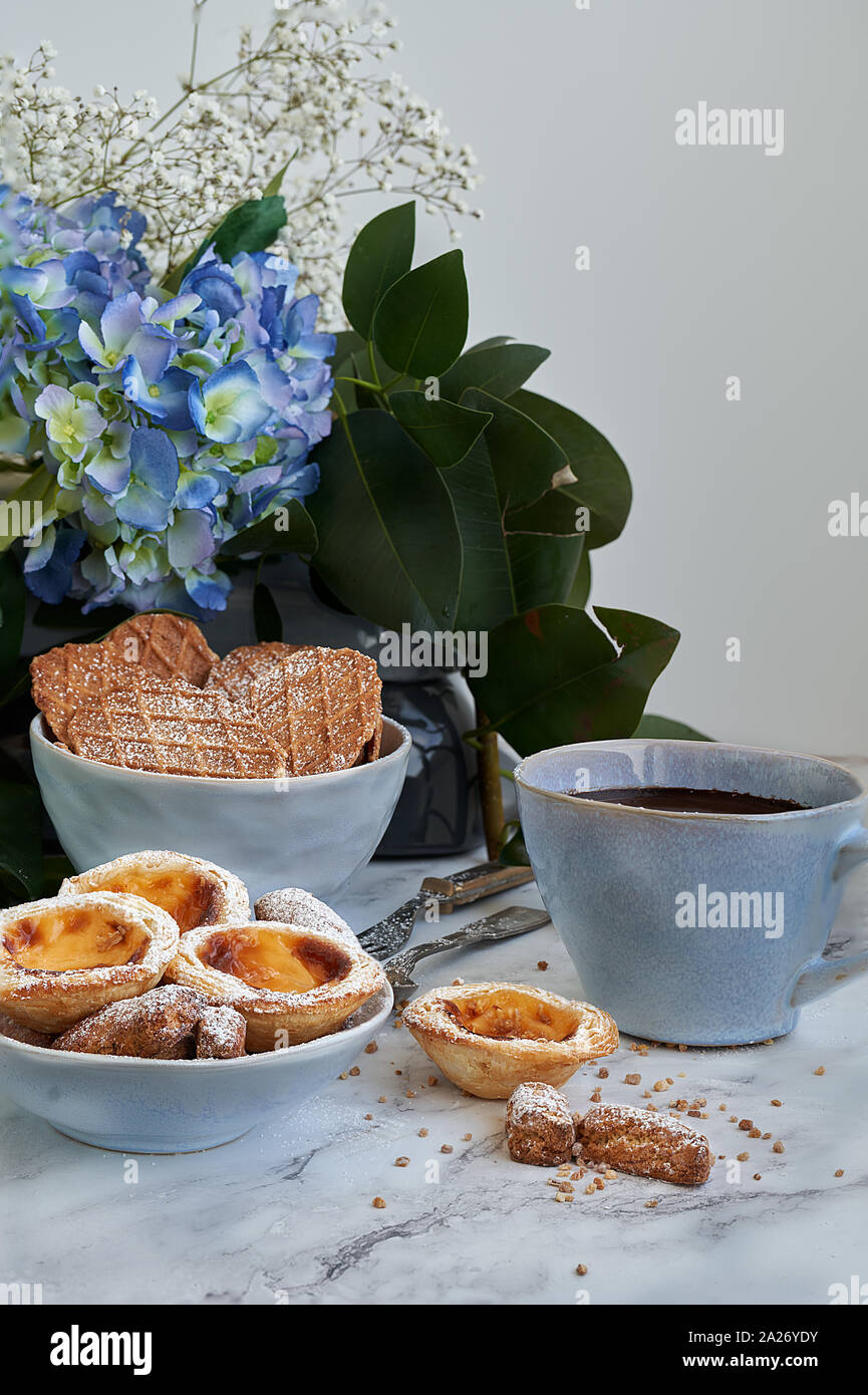 Pasta sfoglia e crema inglese dolci accompagnati da una tazza di  cioccolato. Marmo bianco sullo sfondo blu e fiori Foto stock - Alamy