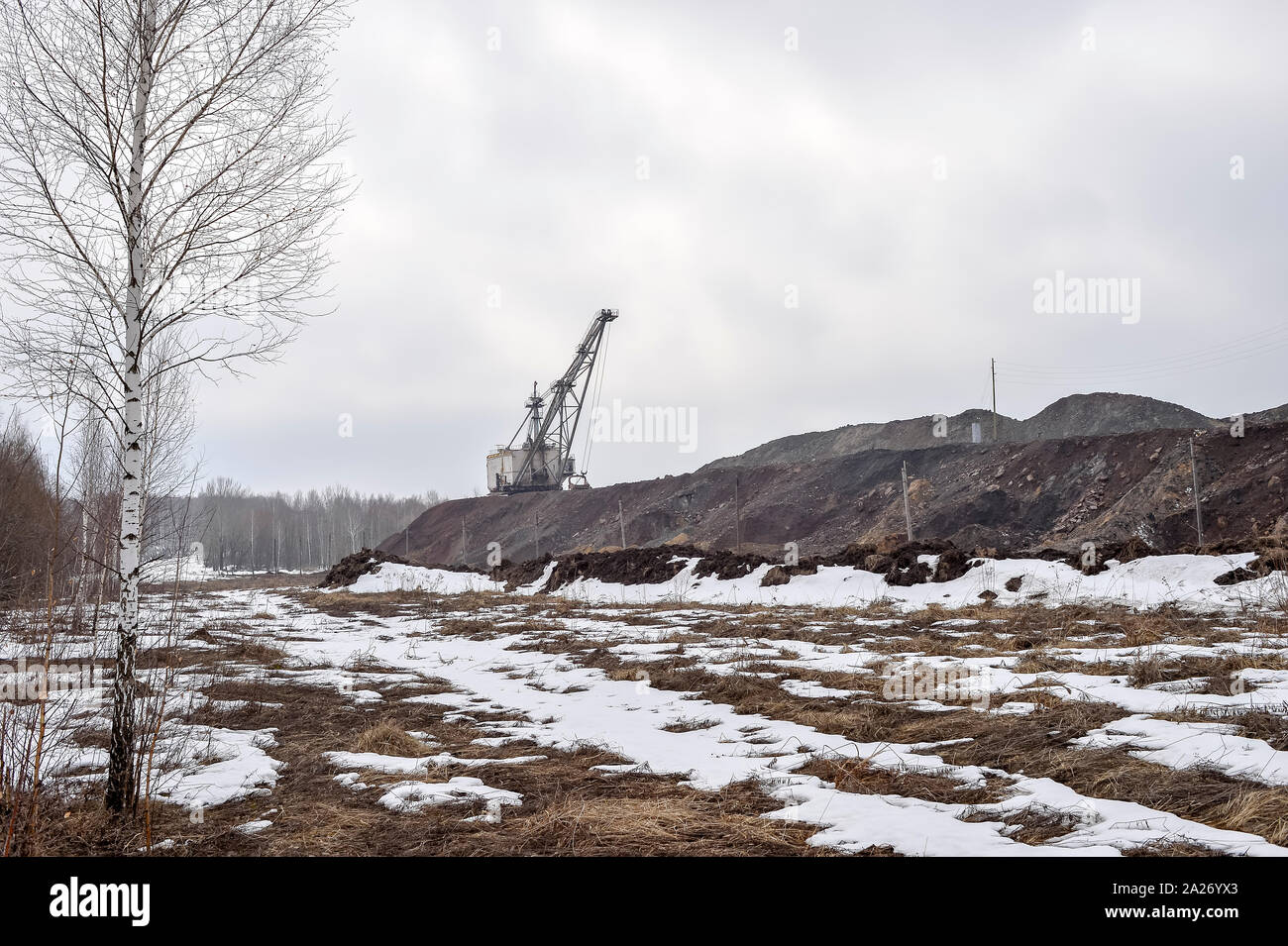 Paesaggio industriale sotto forma di discariche di quarzite, un enorme escavatore a piedi e i resti della foresta in primo piano. Copia dello spazio. Foto Stock