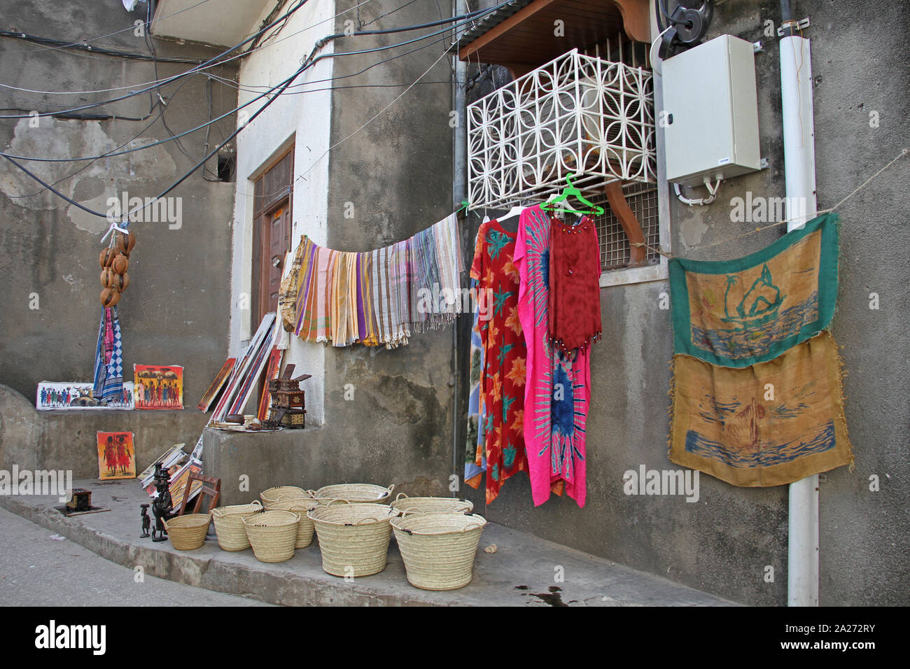 Dipinti, percussione strumenti battagli, cestelli e diversi indumenti che vengono venduti al di fuori di una casa di paese in pietra, Zanzibar, isola di Unguja, Tanzania. Foto Stock