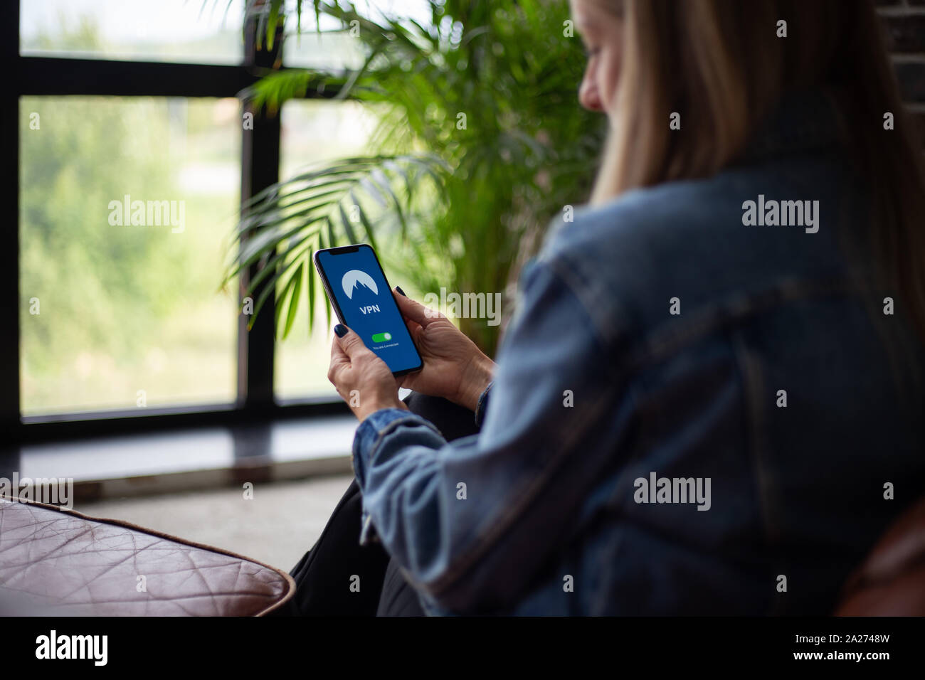 Donna seduta sul divano e cercando una nuova app VPN per la privacy Foto Stock