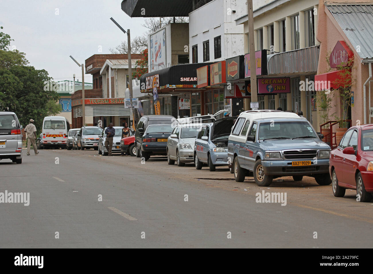 Strada con traffico parcheggiate e negozi, Zimbabwe. Foto Stock
