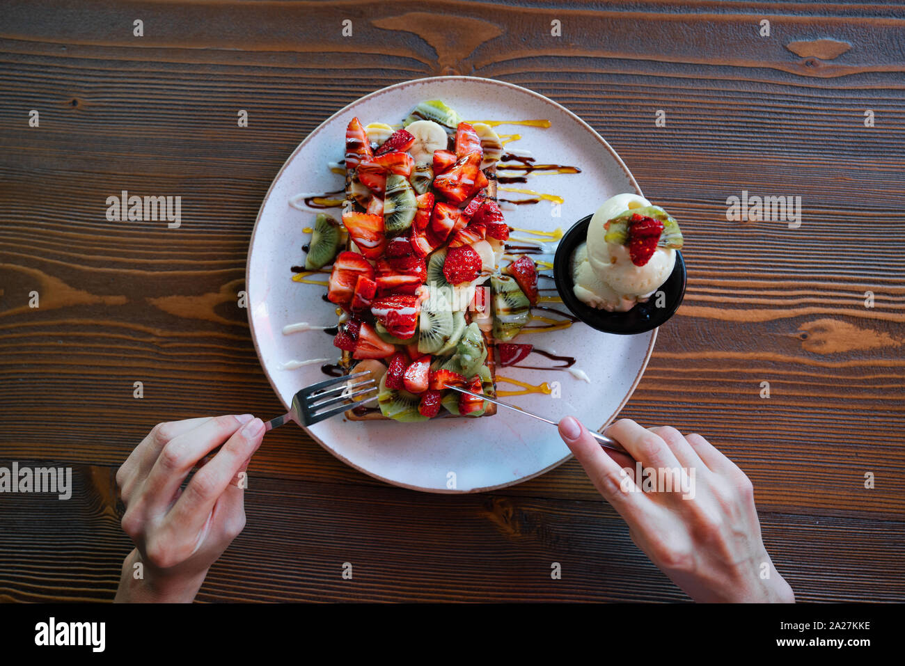 Donna mangiare gustosi e colorati i waffle belgi con fruites e cioccolato su un tavolo di legno. Foto Stock